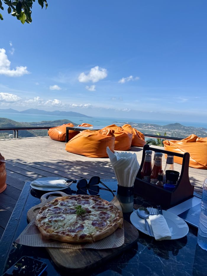Pizza on a table beside orange beanbags at a Koh Samui viewpoint restaurant overlooking the sea