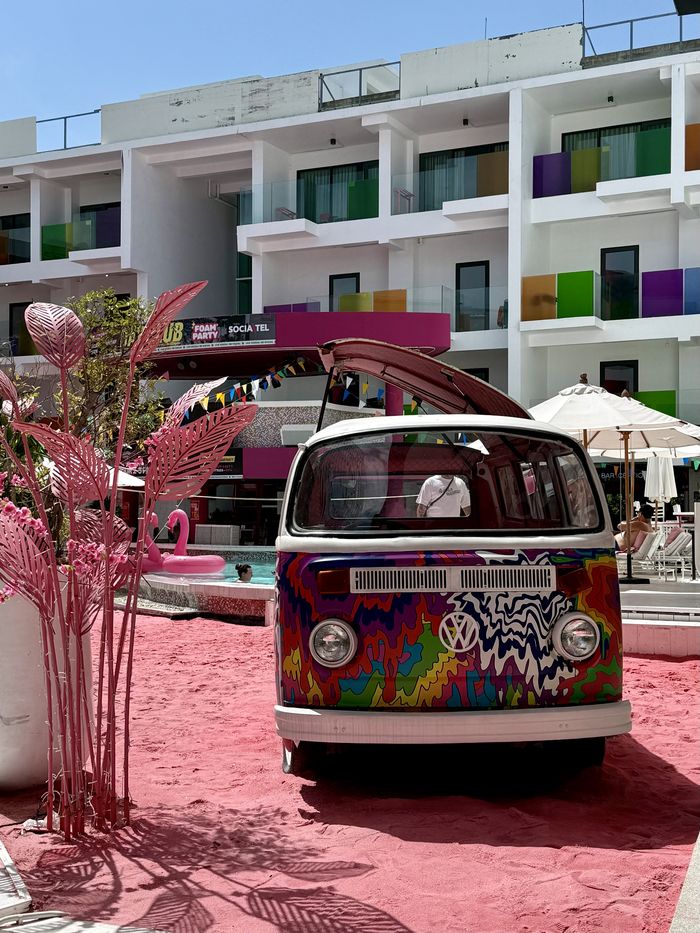 Painted VW camper van parked on pink sand in front of a colourful Koh Samui hotel day club